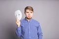 Young man taking off plain white mask revealing face, gray background Royalty Free Stock Photo