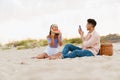 Young man taking photo of his girlfriend during picnic on beach Royalty Free Stock Photo