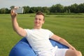 Young man taking selfie while sitting on bean bag chair outdoors Royalty Free Stock Photo