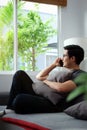 Young man talking on mobile phone and looking out of window while sitting on sofa Royalty Free Stock Photo