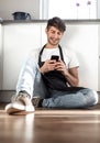 Young man talking on mobile phone sitting on kitchen floor