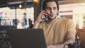 Young man talking mobile phone and using laptop computer in cafe Royalty Free Stock Photo