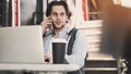 Young man talking mobile phone and using laptop computer in cafe Royalty Free Stock Photo