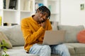 Young man talking on mobile phone and using laptop while sitting on couch at home. Royalty Free Stock Photo