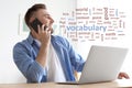 Young man talking on mobile phone while working with laptop at desk, word cloud in front of him Royalty Free Stock Photo