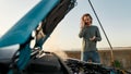 Young man talking on the phone with car service, assistance or tow truck while standing near his broken car with open Royalty Free Stock Photo