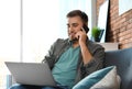 Young man talking on phone while using laptop in room Royalty Free Stock Photo