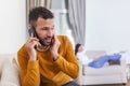 Young Man Talking Privately On Cell Phone While His Wife is watching tv in the back. Handsome young man cheating on girlfriend Royalty Free Stock Photo