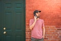 Young man talking with smartphone in front of a brick wall building in the city.