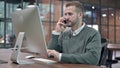 Young Man talking Smartphone while using Desktop Royalty Free Stock Photo