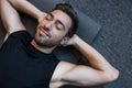 Young man in tanktop lying on a yoga mat with eyes closed and hands