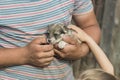 a young man with tanned arms is holding a very small puppy. the baby is petting him. daylight. close-up