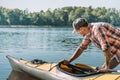 Young man in cap and shirt pushes a kayak in the water of lake.