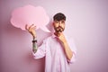 Young man with tattoo holding cloud speech bubble standing over isolated pink background serious face thinking about question,