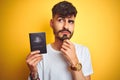 Young man with tattoo wearing Australia Australian passport over isolated yellow background serious face thinking about question,