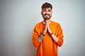 Young man with tattoo wearing orange sweater standing over isolated white background praying with hands together asking for