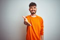 Young man with tattoo wearing orange sweater standing over isolated white background smiling friendly offering handshake as