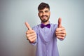 Young man with tattoo wearing purple shirt and bow tie over isolated white background approving doing positive gesture with hand, Royalty Free Stock Photo