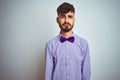 Young man with tattoo wearing purple shirt and bow tie over isolated white background depressed and worry for distress, crying Royalty Free Stock Photo