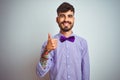 Young man with tattoo wearing purple shirt and bow tie over isolated white background doing happy thumbs up gesture with hand Royalty Free Stock Photo