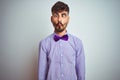 Young man with tattoo wearing purple shirt and bow tie over isolated white background making fish face with lips, crazy and Royalty Free Stock Photo