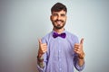 Young man with tattoo wearing purple shirt and bow tie over isolated white background success sign doing positive gesture with Royalty Free Stock Photo