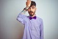 Young man with tattoo wearing purple shirt and bow tie over isolated white background surprised with hand on head for mistake,