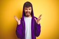 Young man with tattoo wearing purple sweatshirt with hood over isolated yellow background celebrating mad and crazy for success