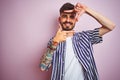 Young man with tattoo wearing striped shirt standing over isolated pink background smiling making frame with hands and fingers Royalty Free Stock Photo