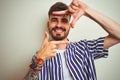 Young man with tattoo wearing striped shirt standing over isolated white background smiling making frame with hands and fingers Royalty Free Stock Photo