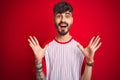 Young man with tattoo wearing striped t-shirt standing over isolated red background celebrating crazy and amazed for success with Royalty Free Stock Photo