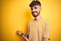 Young man with tattoo wearing striped t-shirt standing over isolated yellow background Inviting to enter smiling natural with open Royalty Free Stock Photo