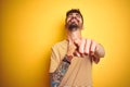 Young man with tattoo wearing striped t-shirt standing over isolated yellow background laughing at you, pointing finger to the Royalty Free Stock Photo