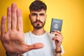 Young man with tattoo wearing United States USA passport over isolated yellow background with open hand doing stop sign with Royalty Free Stock Photo