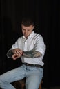 Young man with tattoos and wristwatch sitting on stool against dark background Royalty Free Stock Photo