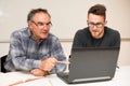 Young man teaching eldery man of usage of computer. Intergenerational transfer of computer skills.