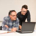 Young man teaching eldery man of usage of computer. Intergenerational transfer of computer skills. Royalty Free Stock Photo