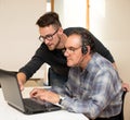 Young man teaching eldery man of usage of computer. Intergenerational transfer of computer skills. Royalty Free Stock Photo