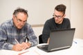 Young man teaching eldery man of usage of computer. Intergenerational transfer of computer skills. Royalty Free Stock Photo