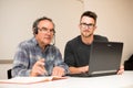 Young man teaching eldery man of usage of computer. Intergenerational transfer of computer skills. Royalty Free Stock Photo