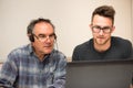 Young man teaching eldery man of usage of computer. Intergenerat Royalty Free Stock Photo