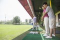 Young man teaching his girlfriend how to hit golf balls, arm around, side view Royalty Free Stock Photo