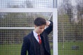 A young man, a teenager, in a classic suit. It is in the football goal. He leaned against the bar with his hand, and laid his head
