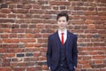 A young man, a teenager, in a classic suit. Pondering is standing in front of the old wall of red brick, putting his hands in his Royalty Free Stock Photo