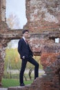 A young man, a teenager, in a classic suit. Pondering is standing in front of the old wall of red brick, putting his hands in his Royalty Free Stock Photo