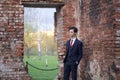 A young man, a teenager, in a classic suit. Pondering is standing in front of the old wall of red brick, putting his hands in his Royalty Free Stock Photo