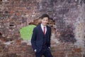 A young man, a teenager, in a classic suit. Pondering is standing in front of the old wall of red brick, putting his hands in his Royalty Free Stock Photo