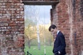 A young man, a teenager, in a classic suit. Pondering is standing in front of the old wall of red brick, putting his hands in his Royalty Free Stock Photo