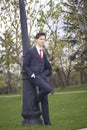 A young man, a teenager, in a classic suit. Relying on a vintage lantern in the park. Put your hands in your pockets.