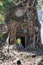 young man, the teenager at an entrance to the destroyed covered with roots of trees temple Prasat Chrap in the Koh Ker temple com